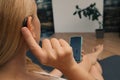 Hearing impaired woman working with smartphone. Close up of blonde woman wearing hearing aid on ear and pressing button while