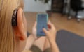 Hearing impaired woman working with smartphone. Close up of blonde woman wearing hearing aid on ear and pressing button while