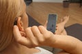 Hearing impaired woman working with smartphone. Close up of blonde woman wearing hearing aid on ear and pressing button while