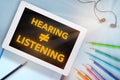 Hearing not equal listening written on computer digital tablet  with coloured pencil and earphone Royalty Free Stock Photo