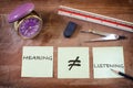 Hearing not equal listening written on sticky notes with alarm clock on wooden table Royalty Free Stock Photo