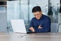 Heart attack at work. A young Asian man is sitting at a desk in the office, holding his heart Royalty Free Stock Photo