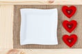 Heart on a background of wood covered with burlap, white square plate a card for Valentine`s Day.