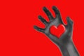 Heart in a black gloved hand isolated on red