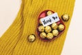 Heart box of golden premium chocolate sweets with thank you tag above woolen mustard color scarf.