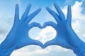 Heart build doctor hands in medical surgical gloves on sky clouds background Royalty Free Stock Photo