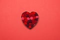 Heart cookie cutter full of terry fabric balls centred on red paper background. Valentines idea