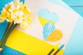 heart cut out of paper and painted in blue and yellow colors and yellow spring flowers on wooding back. Creativity Royalty Free Stock Photo