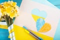 heart cut out of paper and painted in blue and yellow colors and yellow spring flowers on wooding back. Creativity Royalty Free Stock Photo