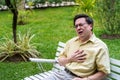 Heart disease,Asian senior man holding his chest and feeling pain suffering from heart attack sitting on armchair outdoor at the g Royalty Free Stock Photo