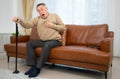 senior guy sits on a sofa with a walking stick in his living room at home Royalty Free Stock Photo