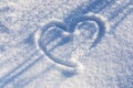 Heart drawing on white snow with diagonal dark blue shadows. Concept of Valentine day