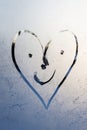 Heart with a drawn face with voices and smile on frosty glass in winter with a finger, heart emoticon drawing by February 14 on