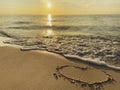 Heart drawn on a sandy beach by the ocean background of an incredibly beautiful sunset, sunrise. White foam of sea wave Royalty Free Stock Photo