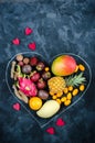 Heart from exotic tropical fruits on dark background. Pineapple, mango, passion fruit, tamarind, granadilla, kumquat, lychee,