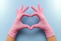  Heart gesture with hands in pink latex protective gloves on a blue background.