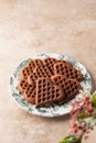 Heart form chocolate waffle cookies in festive plate for Valentine's day with tflowers on beige background, text