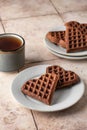 Heart form chocolate waffle cookies in white plate for Valentine's day with tea on pink tileba ckground. Sweet