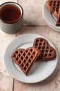 Heart form chocolate waffle cookies in white plate for Valentine& x27;s day with tea on pink tileba ckground. Sweet