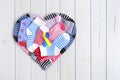 Heart formed by different striped and colored children`s socks on a wooden background. In the center there is a yellow and blue