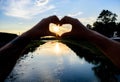 Heart gesture in front of sunset above river. Idea honeymoon travel. Honeymoon summer resort. Romantic date ideas