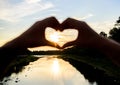 Heart gesture in front of sunset above river. Idea honeymoon travel. Honeymoon summer resort. Romantic date ideas. Hands