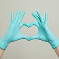Heart from hands in blue doctor gloves on gray background. Medical assistance concept