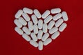 A heart laid out of white pills on a red background, with place for text. Medical heart care concept. White vitamins and calcium.