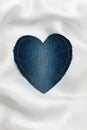 Heart made of denim fabric with yellow stitching on white silk