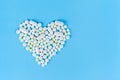 A heart made of different pills on a blue paper background