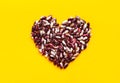 Heart made from dry uncooked red and white speckled beans on bright yellow background. Creative food art poster