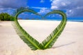Heart made of palm tree leaves on tropical island with overwater bungalows in the background. Royalty Free Stock Photo