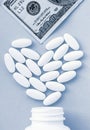 Heart made of pills and money over the neck of a bottle. Expensive medicine and venal love on classic blue background Royalty Free Stock Photo