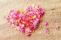 Heart made of pink petals of tropical flowers on the sand, close-up, top view. Royalty Free Stock Photo