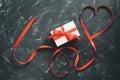 Heart made of red satin ribbon and gift box on black stone background. Valentine`s Day. Top view, flat lay Royalty Free Stock Photo