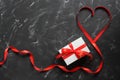 Heart made of red silk ribbon and a gift box on a black stone background. Abstract background for lovers. Top view, flat lay Royalty Free Stock Photo