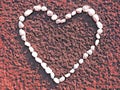 Heart made of small white pebbles on sand in red closeup Royalty Free Stock Photo