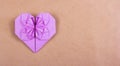 Heart of origami of purple paper on brown recycled paper.