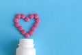 Heart from pink pills next to white bottle on blue background Royalty Free Stock Photo