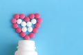 Heart from pink and white pills next to white bottle on blue background Royalty Free Stock Photo