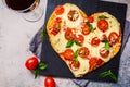 Heart pizza with mozzarella and tomatoes on slate, top view. Valentine`s day date food concept