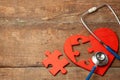 Heart puzzle red and stethoscope on wooden background. Concept diagnosis and treatment of heart disease, medical insurance Royalty Free Stock Photo