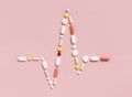 Heart rhythm cardiogram line made of colorful drug pills and capsules on light pink, top view