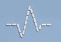 Heart rhythm cardiogram line made of white drug pills on light blue, top view