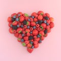 Heart shape of assorted berries on pastel pink background.