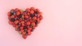 Heart shape of assorted berries on pastel pink background.