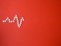 Heart shape and cardiogram made by medical pill on red background.