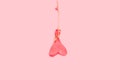 A heart shape deflated pink balloon hanging from a sisal thread on a pink background
