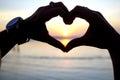 Heart shape with hands gesture. Closeup of a person making love sign in hand with beautiful sunset on the background.