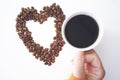 Heart shape made from coffee beans with cup of coffee on white background.